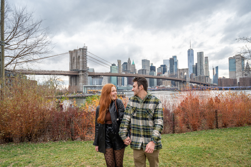 photographing a couple in front of the Manhattan skyline as they get engagement photos in NYC