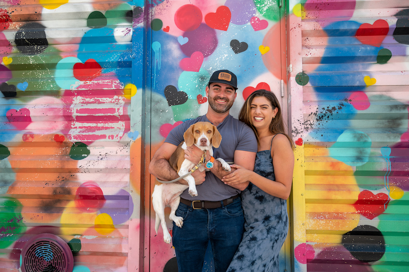 couple posing with their dog in front of a heart mural at the World Trade Center Mural Project