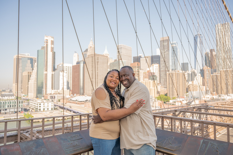 couple posing on the Brooklyn Bridge with the Manhattan skyline behind them