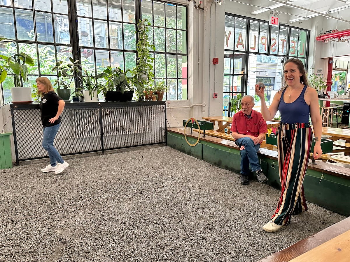 woman in a blue tank top and striped pants playing pétanque at Carreau Club in Industry City to celebrate her birthday in NYC