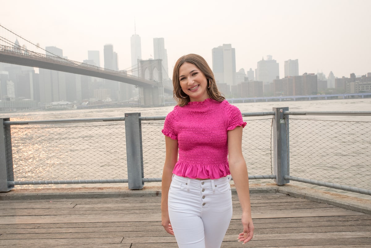 female influencer in a pink shirt walking along the DUMBO waterfront at sunset
